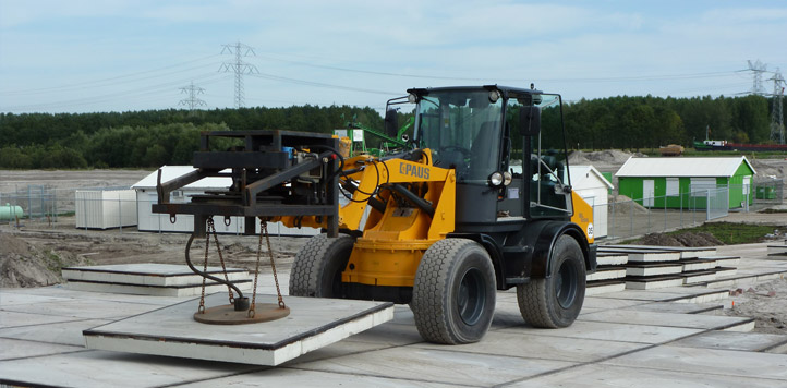 Gele shovel legt met een vacuümhefinstallatie een betonplaat van twee bij twee meter op zijn plek