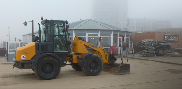 Gele shovel van Schoorl aan het werk bij een strandpaviljoen